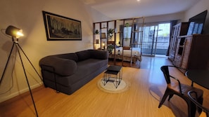 A living room with a sofa, a small table, a floor lamp, a bed with a view, and a wooden cabinet. - Palermo Soho: Up to 4 Pax - Modern with Balcony (Buenos Aires)