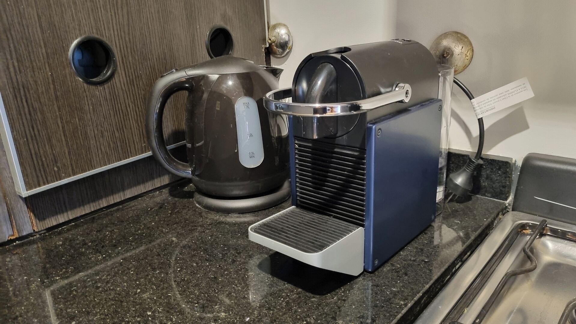 Una cucina con una macchina da caffè, un bollitore e un lavello piccolo.