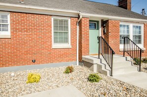 A brick house with a green door, white windows, and a concrete front porch with steps.