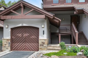 Une maison à deux étages avec une porte de garage marron, des marches en pierre et un escalier en bois.