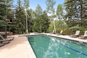 Ein Swimmingpool mit Liegestühlen und einer Terrassenfläche, umgeben von Bäumen und einem Gebäude.