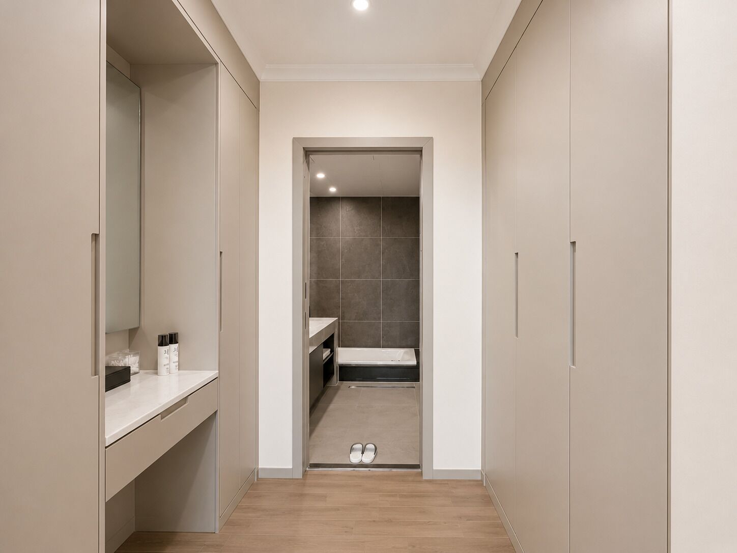 A narrow hallway leading to a bathroom with a shower, a toilet, and a sink.