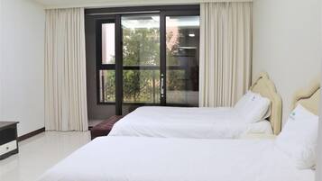 A hotel room with two beds, a window with curtains, a bench, and a desk.
