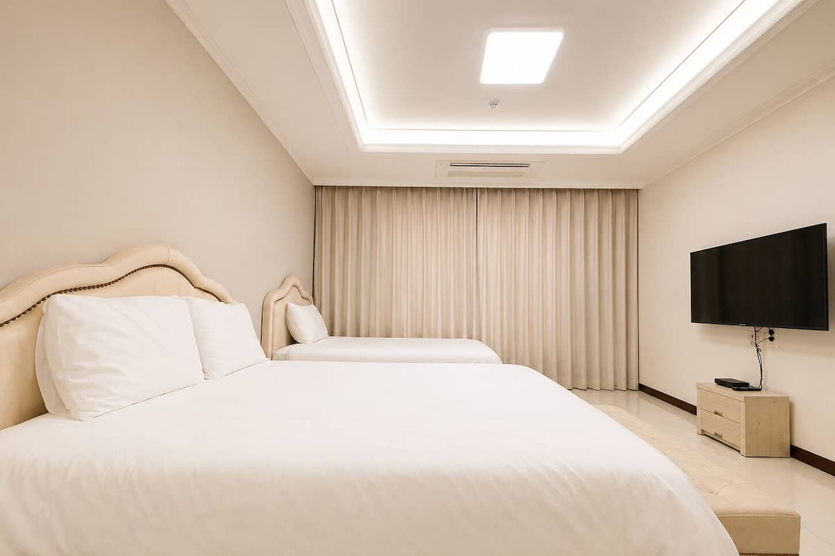 Modernilla designilla sisustettu hotellihuone, jossa on suuri sänky päätyineen, seinälle asennettu taulutelevisio ja kattovalaisin.