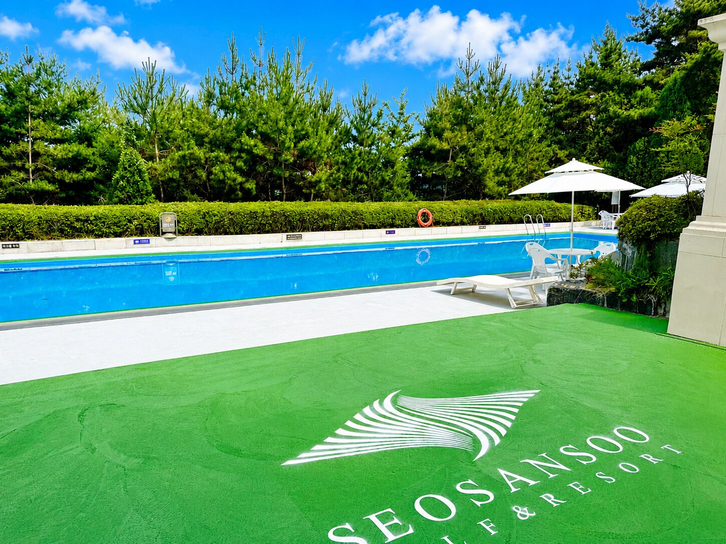 Ein Swimmingpool mit grüner Rasenfläche, weißen Liegestühlen und Sonnenschirmen.