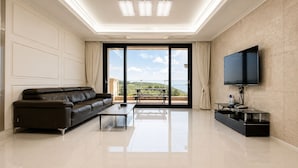 A modern living room with a sofa, a flat-screen TV, and a balcony with a table and chairs. - Seosansoo Golf & Resort (Seosan)