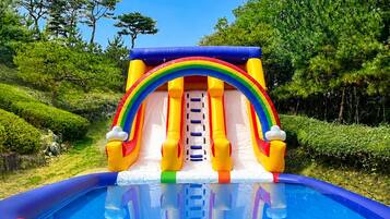 An inflatable slide with a rainbow arch and a pool at the bottom.