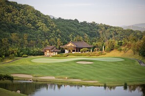 A golf course with a pond, a clubhouse, and a forested hillside. - Seosansoo Golf & Resort (Seosan)