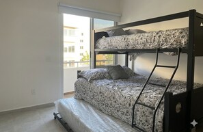 A bunk bed with floral bedding, a window with a view of buildings, and a door. - Bluu lagoon and beach (Mazatlán)