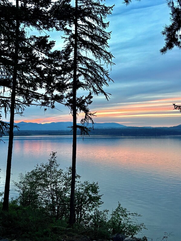 Un lago tranquilo con altos árboles en primer plano y montañas a lo lejos.