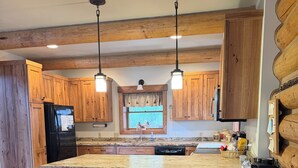 Una cocina con armarios de madera, un refrigerador negro, encimera de granito y una ventana con cortinas.