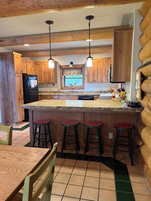 A kitchen with wooden cabinets, a black refrigerator, a granite countertop, and a window with curtains. - Lakefront cabin on Placid Lake.  Hot tub, fire pit, paddleboards. Sleeps 11. (Seeley Lake)