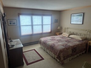A bedroom with a bed, a nightstand, a dresser, a window with blinds, and a framed picture on the wall.