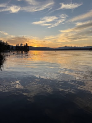 A calm lake at sunset with mountains in the background.