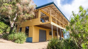 A two-story yellow building with a covered porch, surrounded by vegetation. - Fourlees Breeze - Ocean Views - Sleeps 11 (Point Lookout)