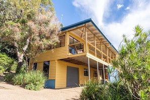 A two-story yellow building with a covered porch, surrounded by vegetation. - Fourlees Breeze - Ocean Views - Sleeps 11 (Point Lookout)