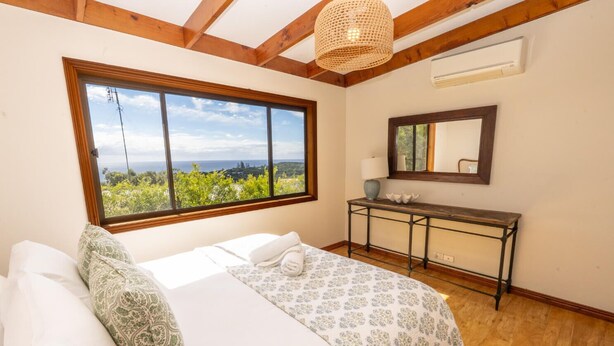 A bedroom with a large window, a bed, a bedside table, and a mirror. - Fourlees Breeze - Ocean Views - Sleeps 11 (Point Lookout)