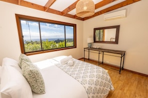 A bedroom with a large window, a bed, a bedside table, and a mirror. - Fourlees Breeze - Ocean Views - Sleeps 11 (Point Lookout)