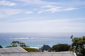 A coastal view with a clear sky, ocean, and a building with a sloped roof. - Fourlees Breeze - Ocean Views - Sleeps 11 (Point Lookout)