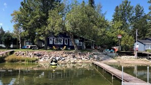A lakeside cabin with a dock, surrounded by trees and a small rocky area.