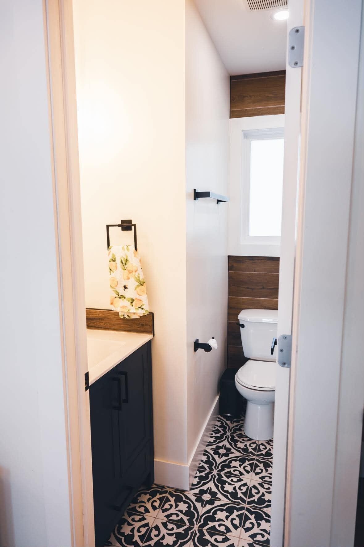 A narrow bathroom with a toilet, a sink with a floral towel, and patterned floor tiles.