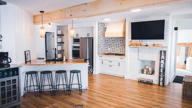 A modern kitchen with a central island, bar stools, a large TV, and a fireplace.