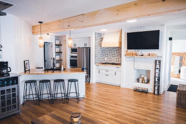 A modern kitchen with a central island, bar stools, a large TV, and a fireplace.