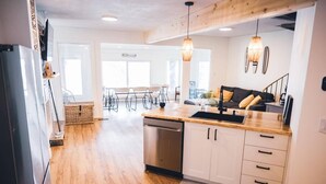 A modern kitchen with wooden flooring, white cabinets, a dishwasher, and pendant lighting.