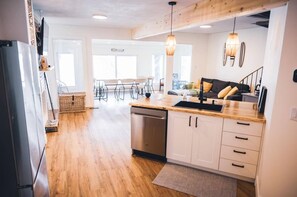 A modern kitchen with wooden flooring, white cabinets, a dishwasher, and pendant lighting.