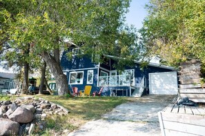 A blue house with a garage, a tree, and outdoor seating.