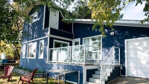 A two-story house with a blue exterior, white trim, a front porch with Adirondack chairs, and a white garage door.