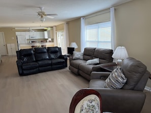 A living room with a black leather sofa, a brown leather sofa, a wooden coffee table, a TV, and a lamp. - Berea Villa's, Polo Ridge, Stunning Courtyard Villa, Golf Cart included! (The Villages)