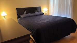A neatly made bed with a dark-colored duvet, two bedside lamps, and a wooden nightstand. - Berea Villa's, Polo Ridge, Stunning Courtyard Villa, Golf Cart included! (The Villages)