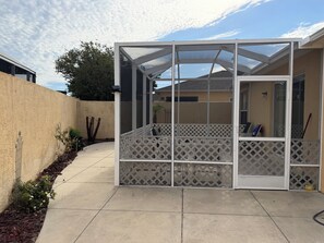 A covered patio area with a lattice fence, a concrete floor, and a view of a house in the background. - Berea Villa's, Polo Ridge, Stunning Courtyard Villa, Golf Cart included! (The Villages)