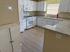 A compact kitchen with white cabinets, a microwave, stove, oven, granite countertop, and a window with blinds. - Berea Villa's, Polo Ridge, Stunning Courtyard Villa, Golf Cart included! (The Villages)