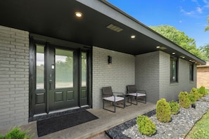 A modern building with a brick facade, a dark-colored entrance door, and a small outdoor seating area with two chairs. - Cozy Luxury Getaway Home (Springfield)