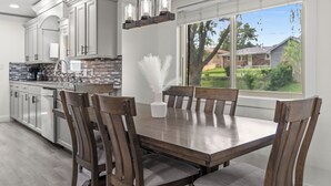 Una cucina moderna con mobili bianchi, un tavolo da pranzo con sedie di legno e vista su un quartiere residenziale attraverso un'ampia finestra.