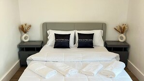 Siististi pedattu sänky valkoisilla lakanoiden kanssa, kaksi yöpöytää koristeellisilla maljakoilla ja harmaa pääty.