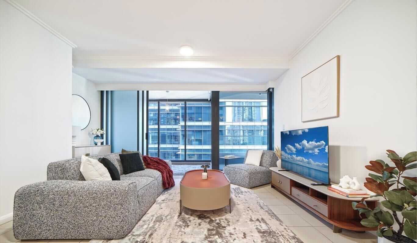 A modern living room with a sofa set, a coffee table, a TV, and a large window with a city view.