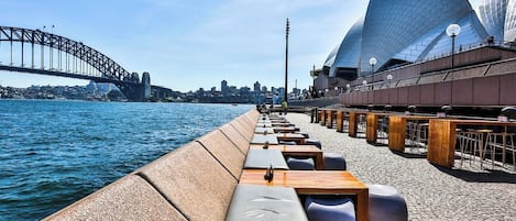 A waterfront promenade with seating, a bridge, and a modern opera house.