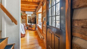 L’intérieur d’une cabane en rondins, avec un escalier en bois, un coin repas comprenant une table et des chaises, et une grande fenêtre offrant une vue panoramique.