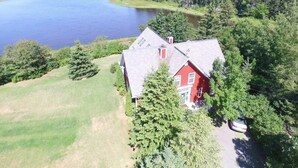 A red house with a sloped roof, surrounded by a forest and a body of water. - Little Shemouge Country Inn (Little Shemogue)