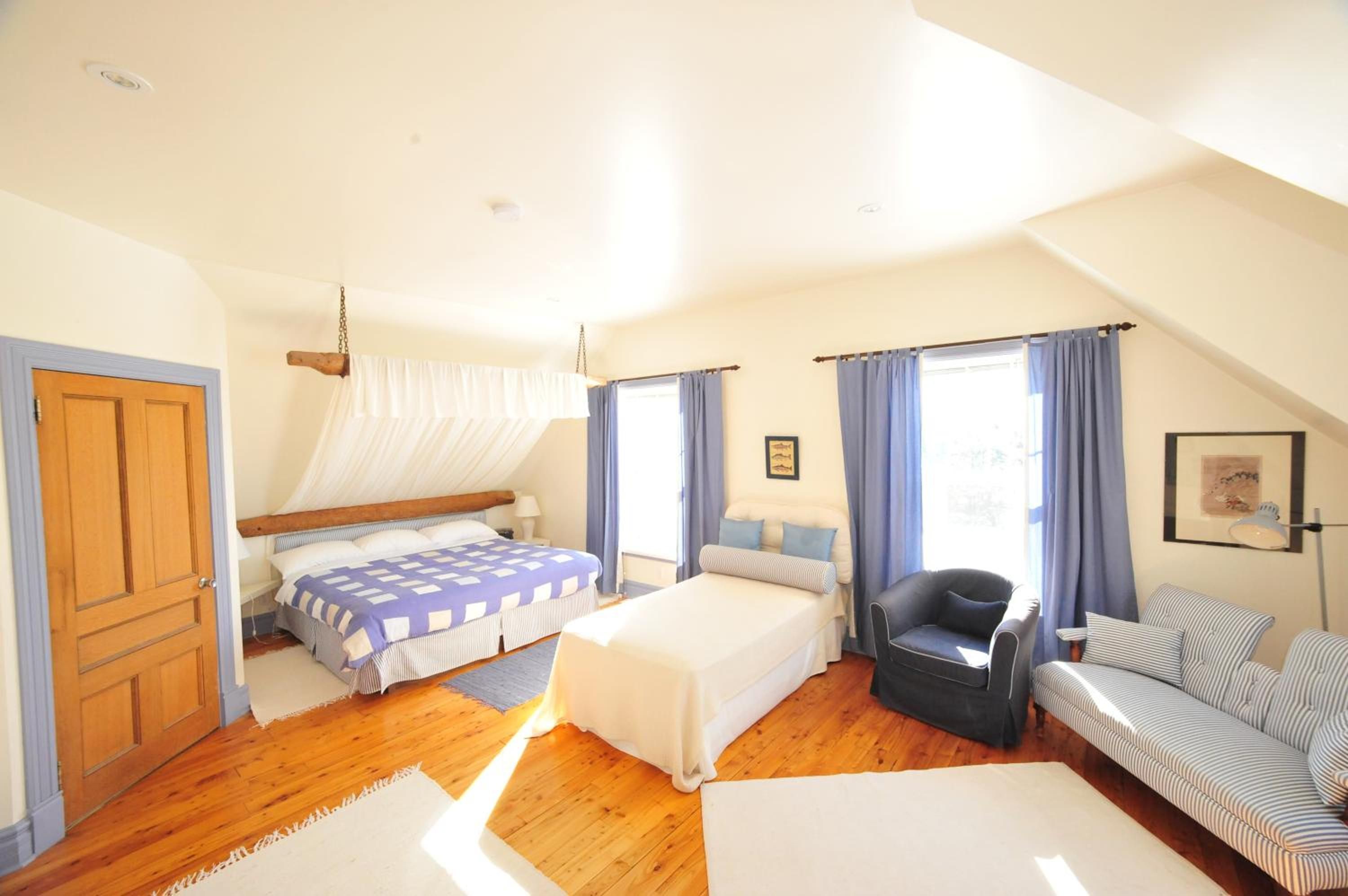 A bedroom with a bed, a chair, a sofa, and a window with curtains.