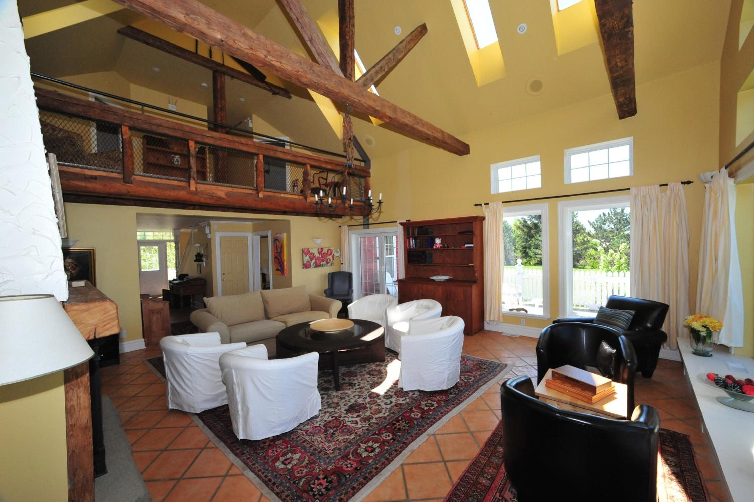 A spacious living area with a high ceiling, wooden beams, a large sofa set, a coffee table, and a bookshelf.