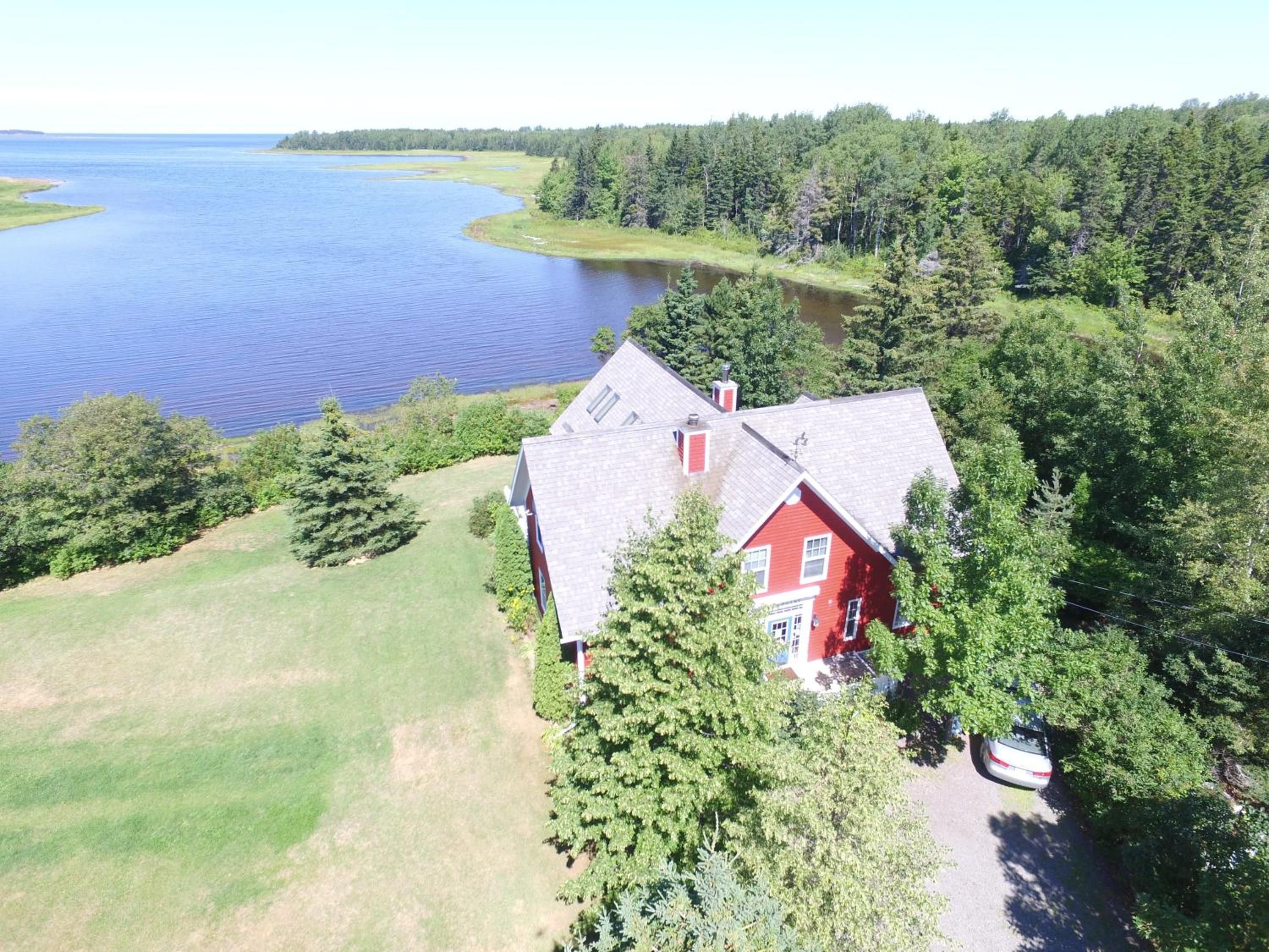 A red house with a sloped roof, surrounded by a forest and a body of water.