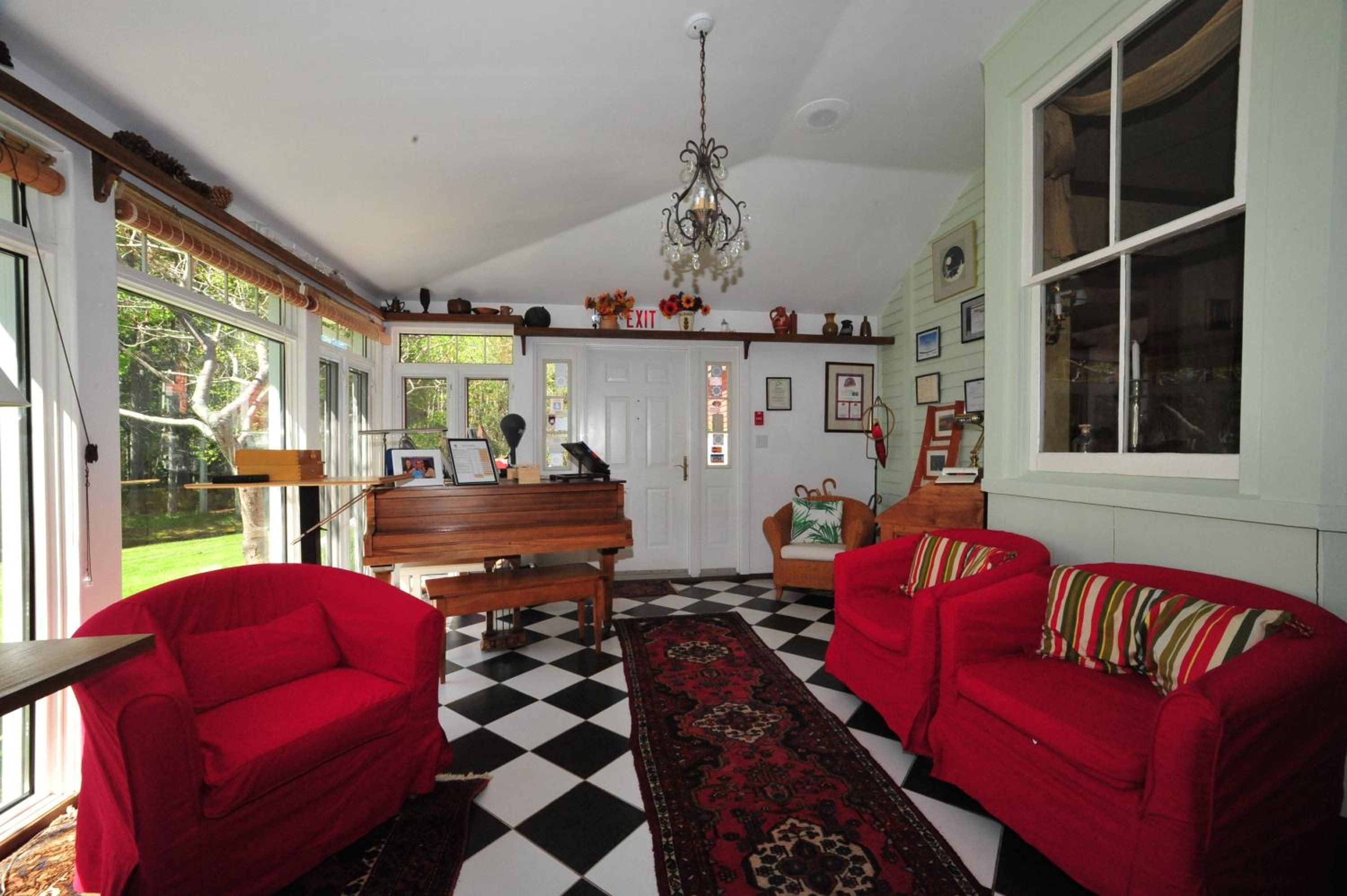 A room with a checkered floor, two red sofas, a piano, and a chandelier.
