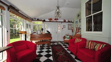 A room with a checkered floor, two red sofas, a piano, and a chandelier.