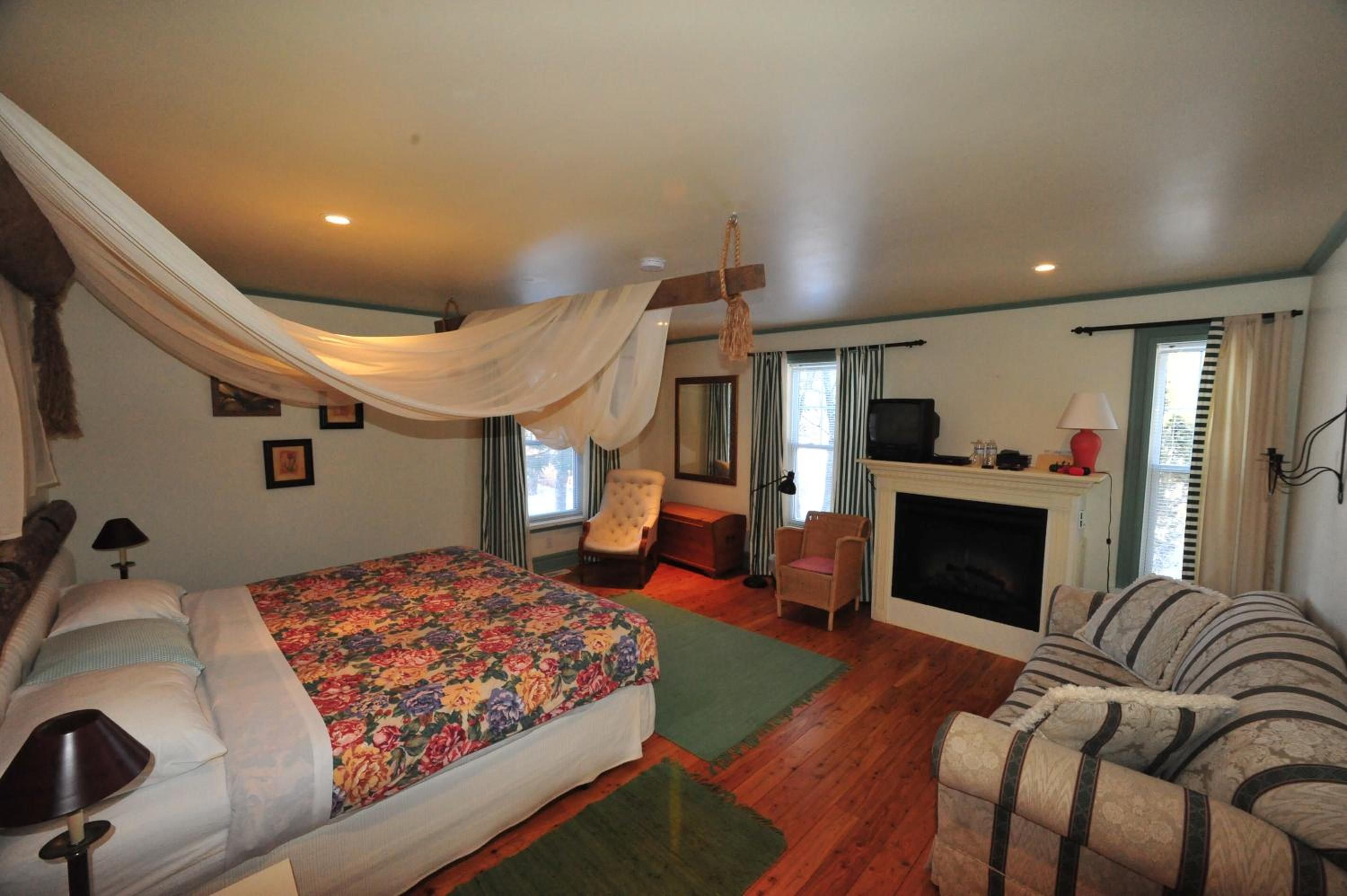 A bedroom with a bed, a chair, a sofa, a fireplace, and a television.