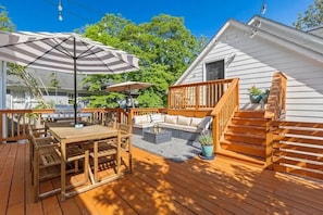 Eine Holzterrasse mit Esstisch, Stühlen, einer Couch und einer Treppe.