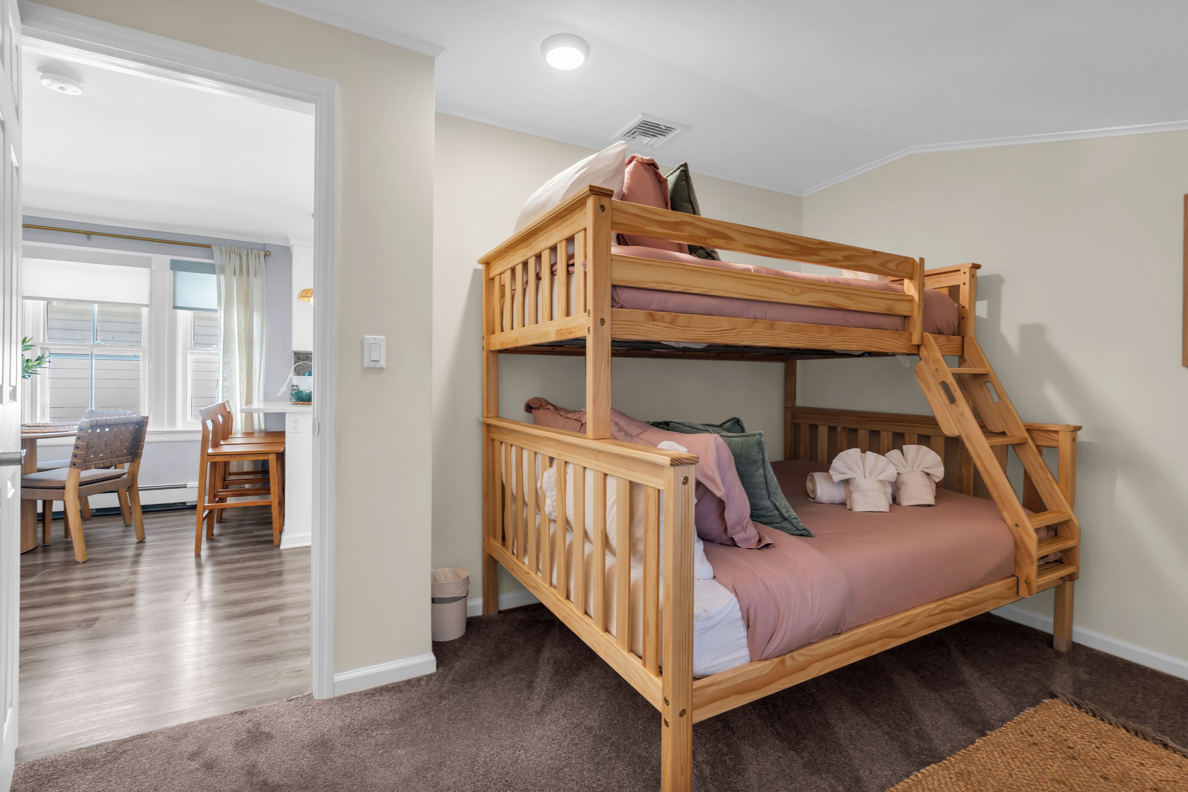 Un lit superposé avec une structure en bois, un bureau avec des chaises et une fenêtre avec des rideaux.